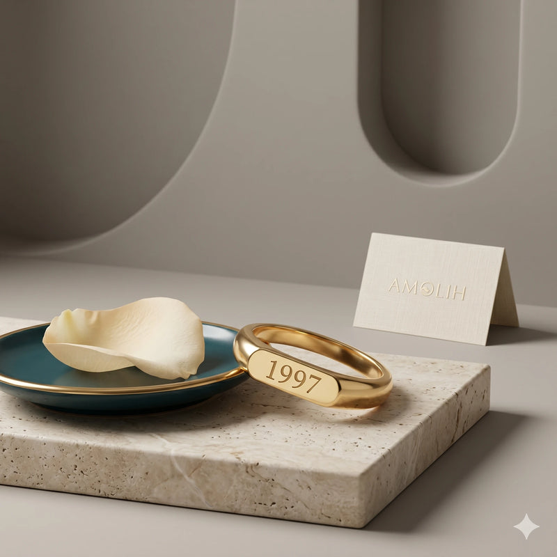 Gold ring with '1997' engraving on a stone surface with a plate and card in the background.